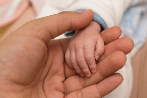 A baby 's hand holding onto the palm of its father.